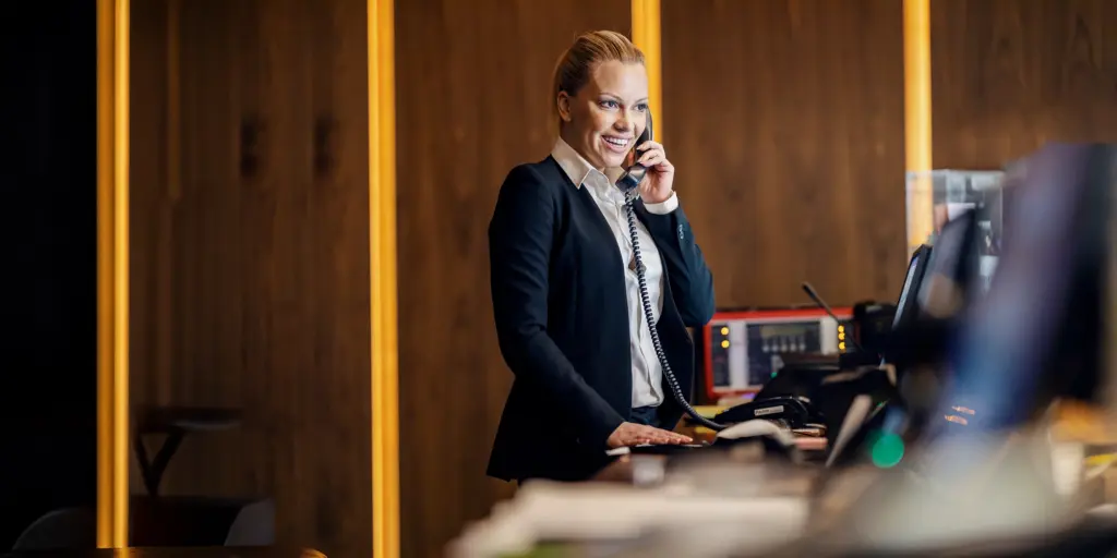 Eine Frau im Anzug telefoniert an einem Empfangstresen und lächelt freundlich.